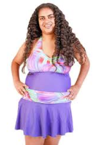 Wman with long brown curly hair wears swimsuit dress in purple with a patterned fabric at top and waist